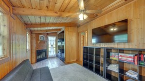A wooden cabin interior with a sofa, fireplace, TV, and shelves with books and games. - < 1 Mi to Casinos: Countryside Louisiana Getaway! (Duson)