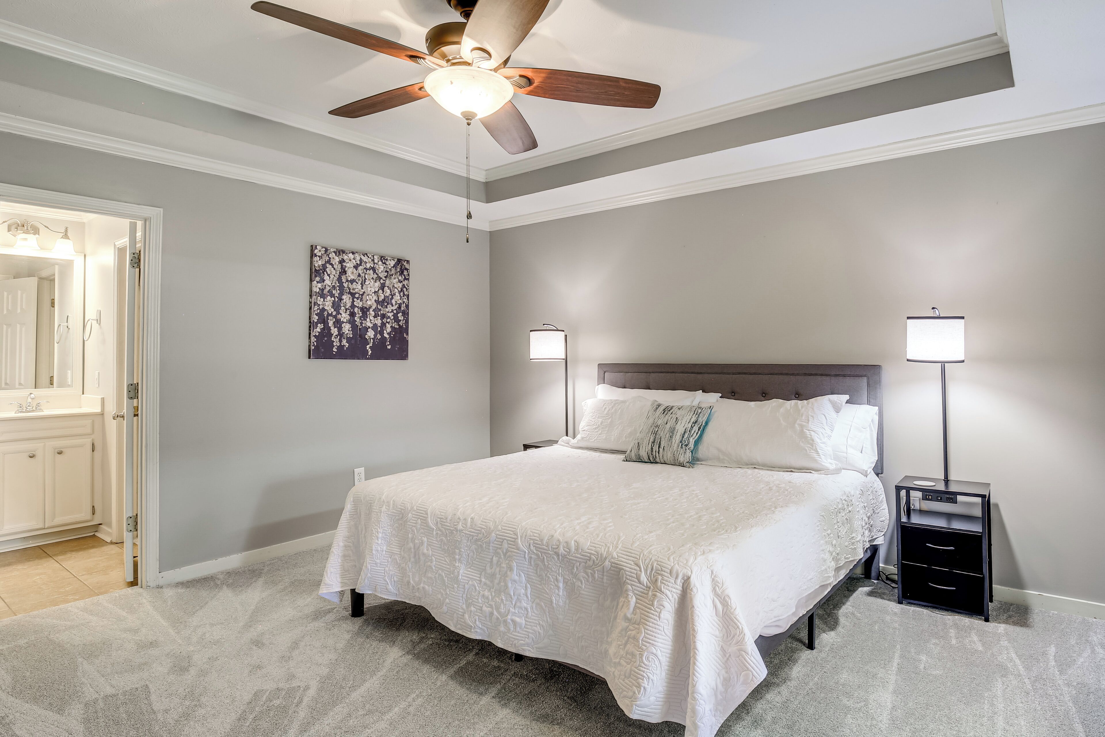 A bedroom with a bed, a ceiling fan, bedside lamps, and a nightstand.