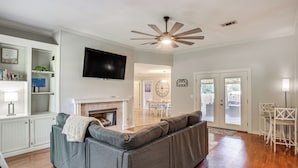 A living room with a gray sectional sofa, a flat-screen TV, a fireplace, and a ceiling fan. - Updated Retreat w/ Outdoor Space in Flowood! (Flowood)