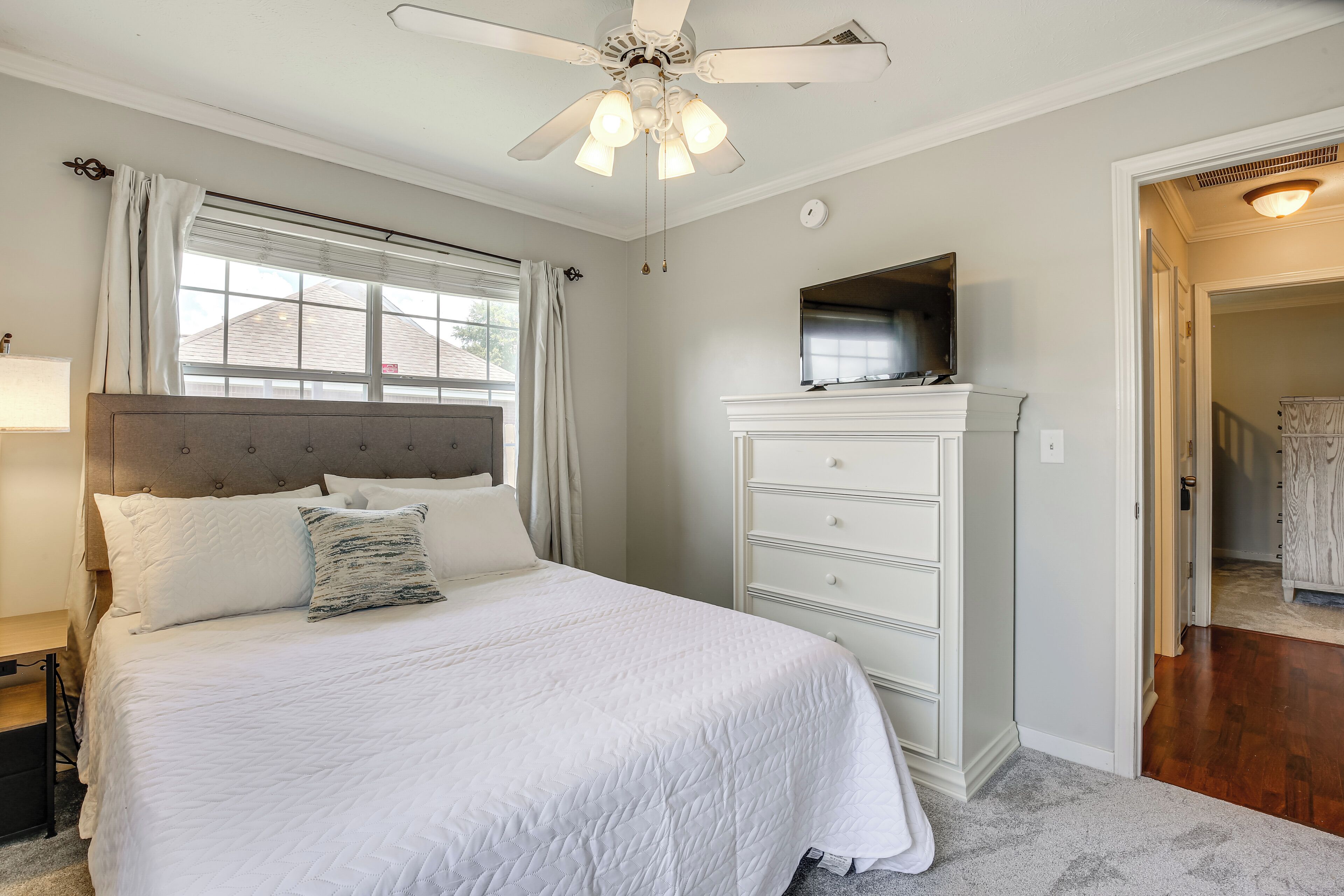A bedroom with a bed, a dresser, a ceiling fan, and a television.