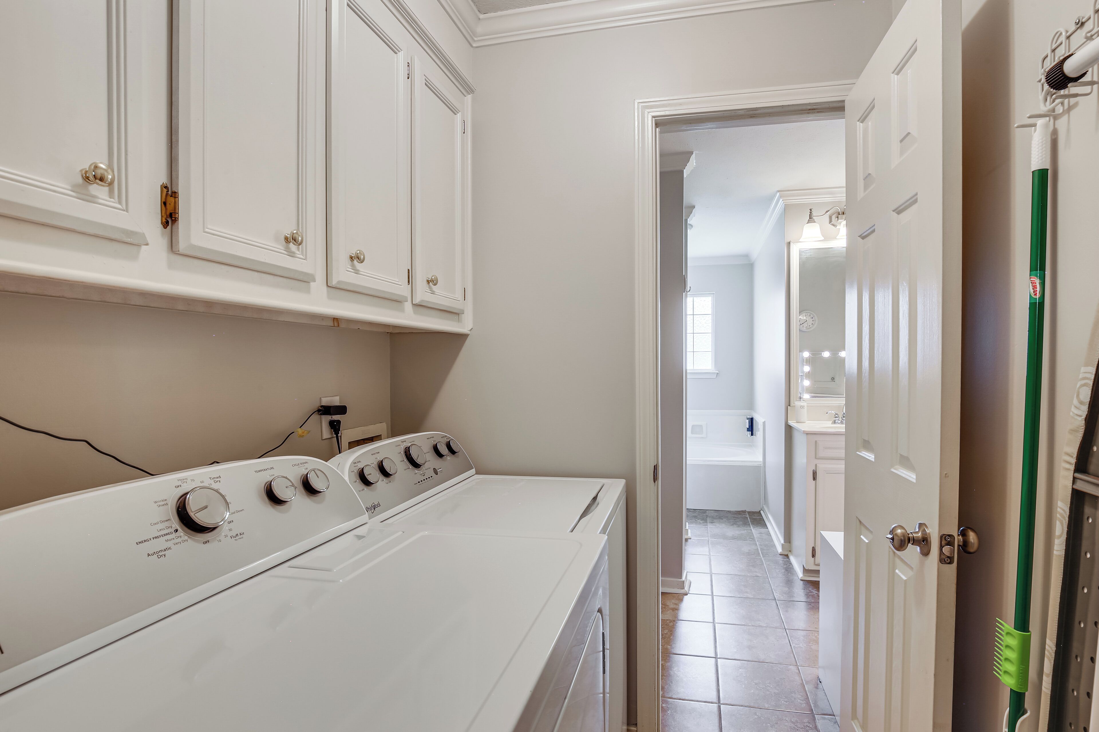 A laundry room with a white washer and dryer, white cabinets, and a green cleaning brush.