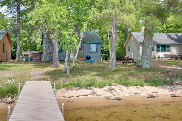 A wooden dock leading to a sandy beach area with several cabins and picnic tables.