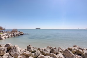 A calm waterfront with large rocks in the foreground and a clear sky.