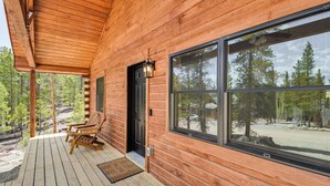 Eine Holzhütte mit Veranda, einer schwarzen Tür und einem großen Fenster mit Blick auf den umliegenden Wald.