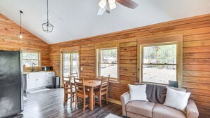 Ein Holzinnenraum einer Hütte, mit Essbereich, Tisch, Stühlen, einer Couch und einer Küchenzeile inklusive Kühlschrank und Schränken.