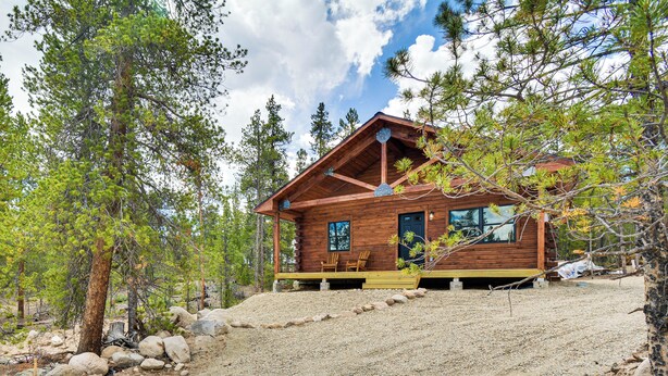 Eine Holzhütte mit Veranda, umgeben von Bäumen und einem Schotterweg.