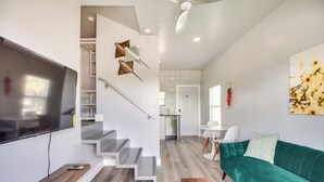A modern living room with a green sofa, a flat-screen TV, and a staircase leading to a kitchen area. - Walk to Daytona Beach & Boardwalk: Apt w/ Balcony (Daytona Beach)