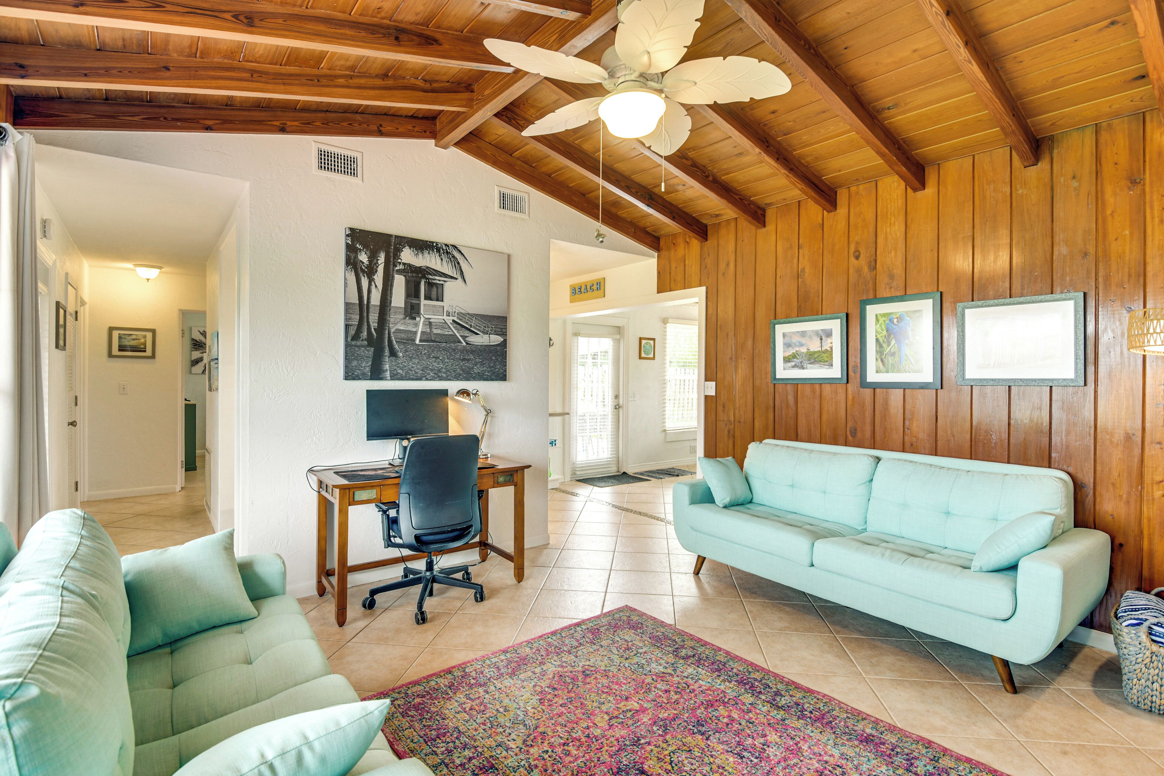 A spacious living room with a light blue sofa, a wooden ceiling, a ceiling fan, and a desk with a computer.