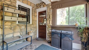 A stone-walled room with a built-in shelf, a pet bowl, a mat, and a window with a view of trees.