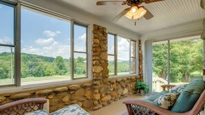A sunroom with large windows, wicker furniture, and a stone wall.
