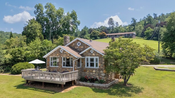 A stone house with a deck, surrounded by a well-maintained lawn and trees.