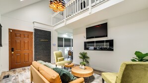 A modern living room with a sofa, armchairs, a round coffee table, a fireplace, and a TV mounted on the wall.