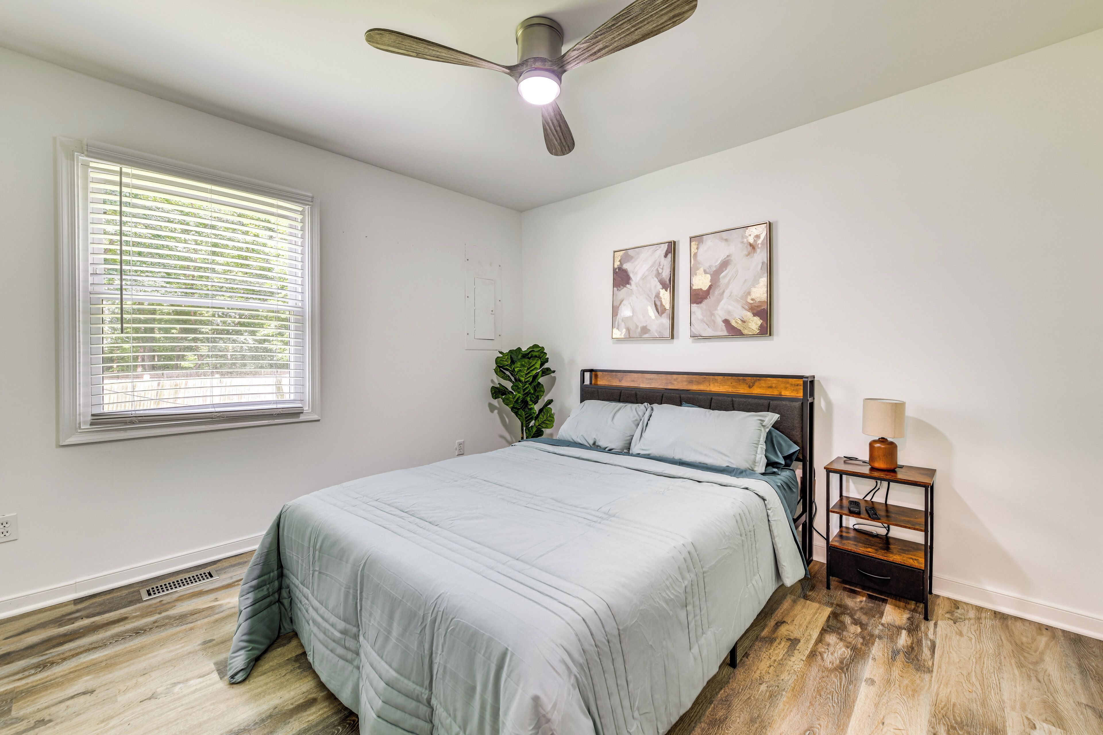 A bedroom with a bed, a ceiling fan, a nightstand, and a window with blinds.