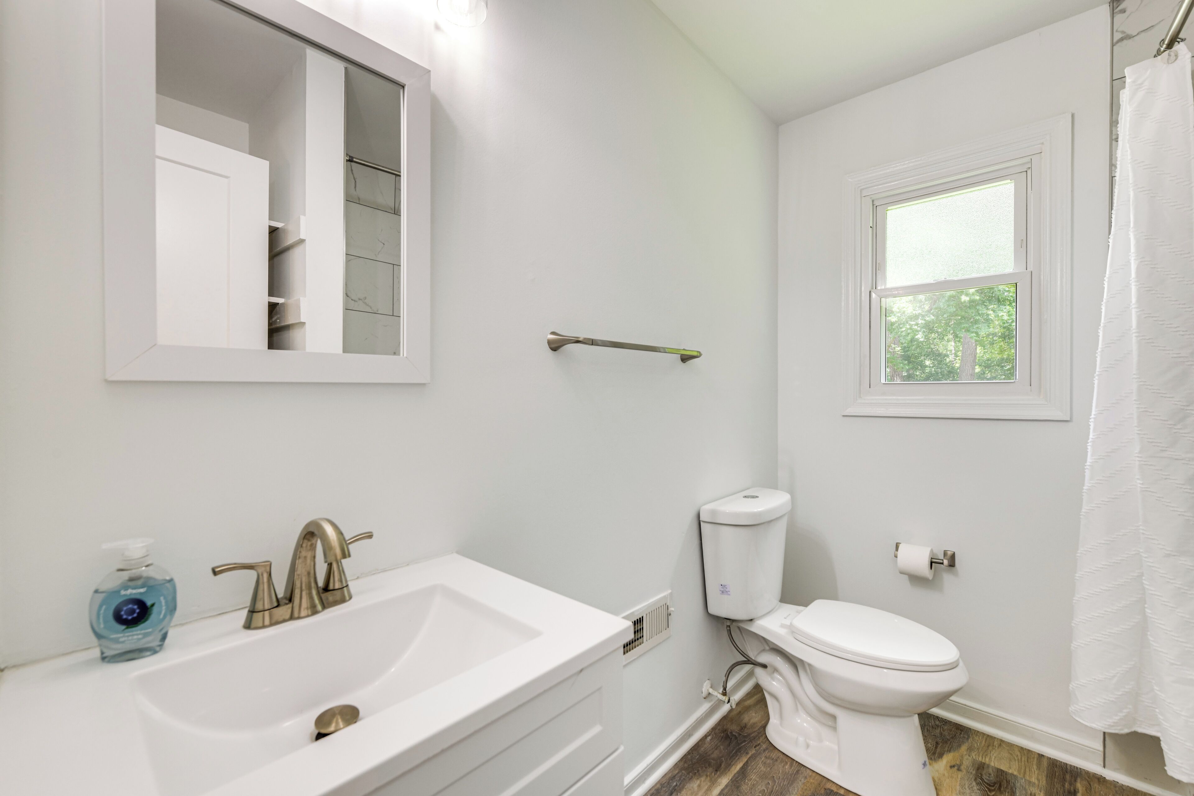 Un baño con lavamanos blanco, inodoro, ventana y cortina de ducha.