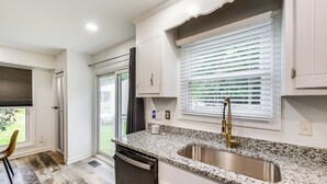 A kitchen with a granite countertop, stainless steel sink, and white cabinets.