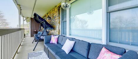 A covered porch with a gray sofa, a stone wall, and a large window.