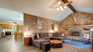 A spacious living area with a large sectional sofa, a round coffee table, and a stone fireplace. - Scenic Asheville Area Retreat: Hot Tub & Game Room (Candler)