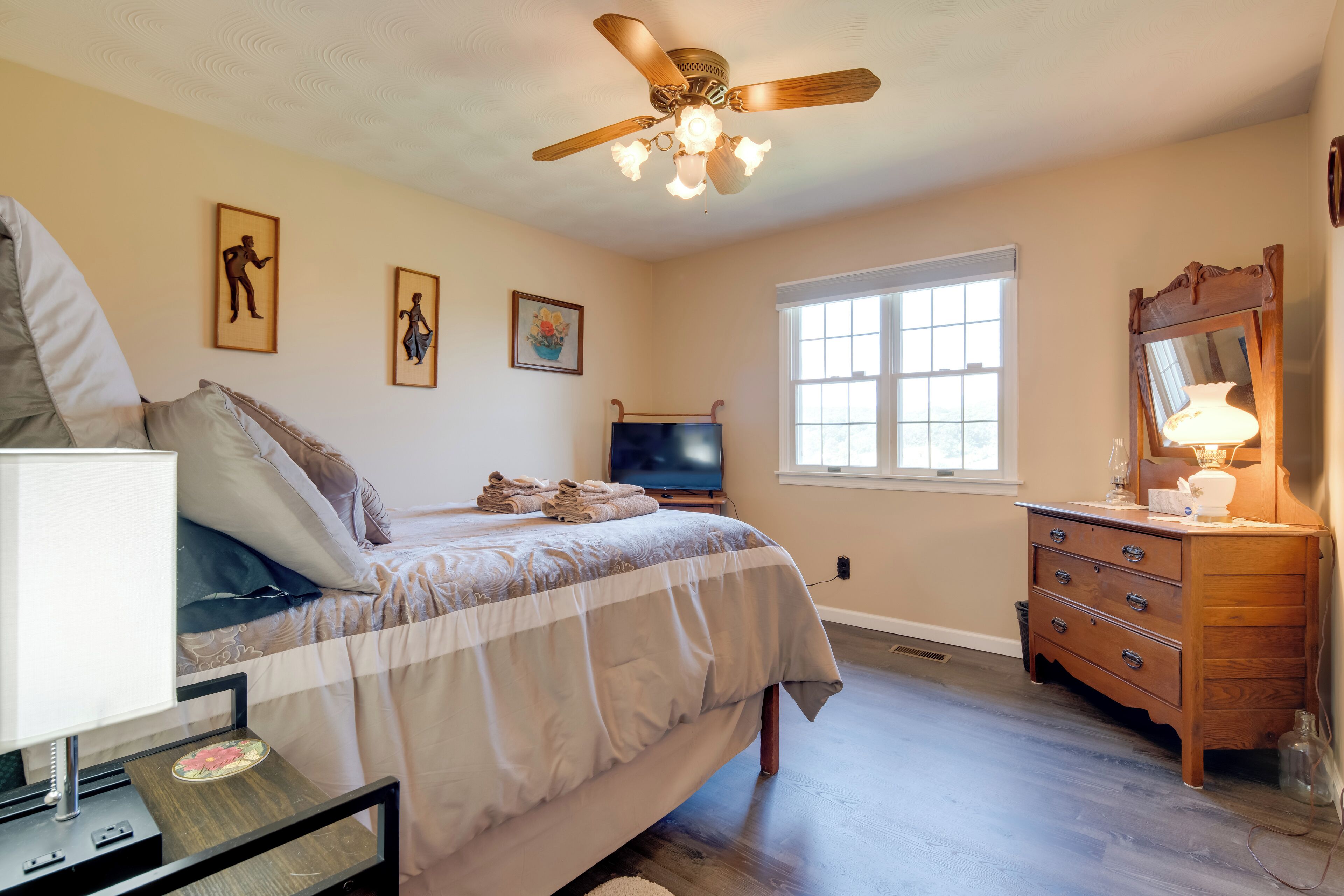 A bedroom with a bed, a dresser, a television, and a ceiling fan.