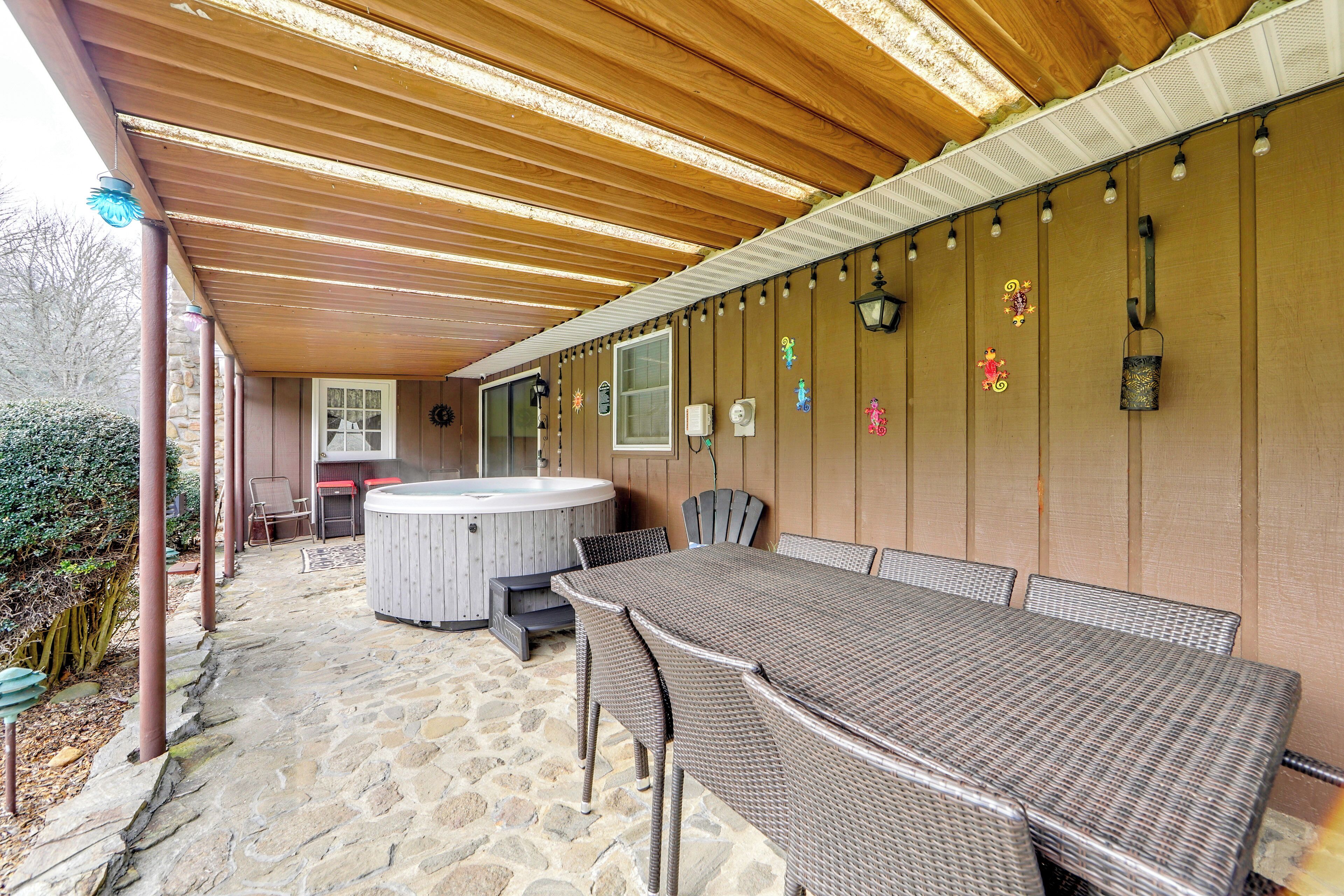 Ein überdachter Patio-Bereich mit Steinboden, Whirlpool, Korbmöbeln und dekorativer Wandbeleuchtung.