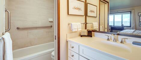 A bathroom with a bathtub, a sink with a mirror, and a window.