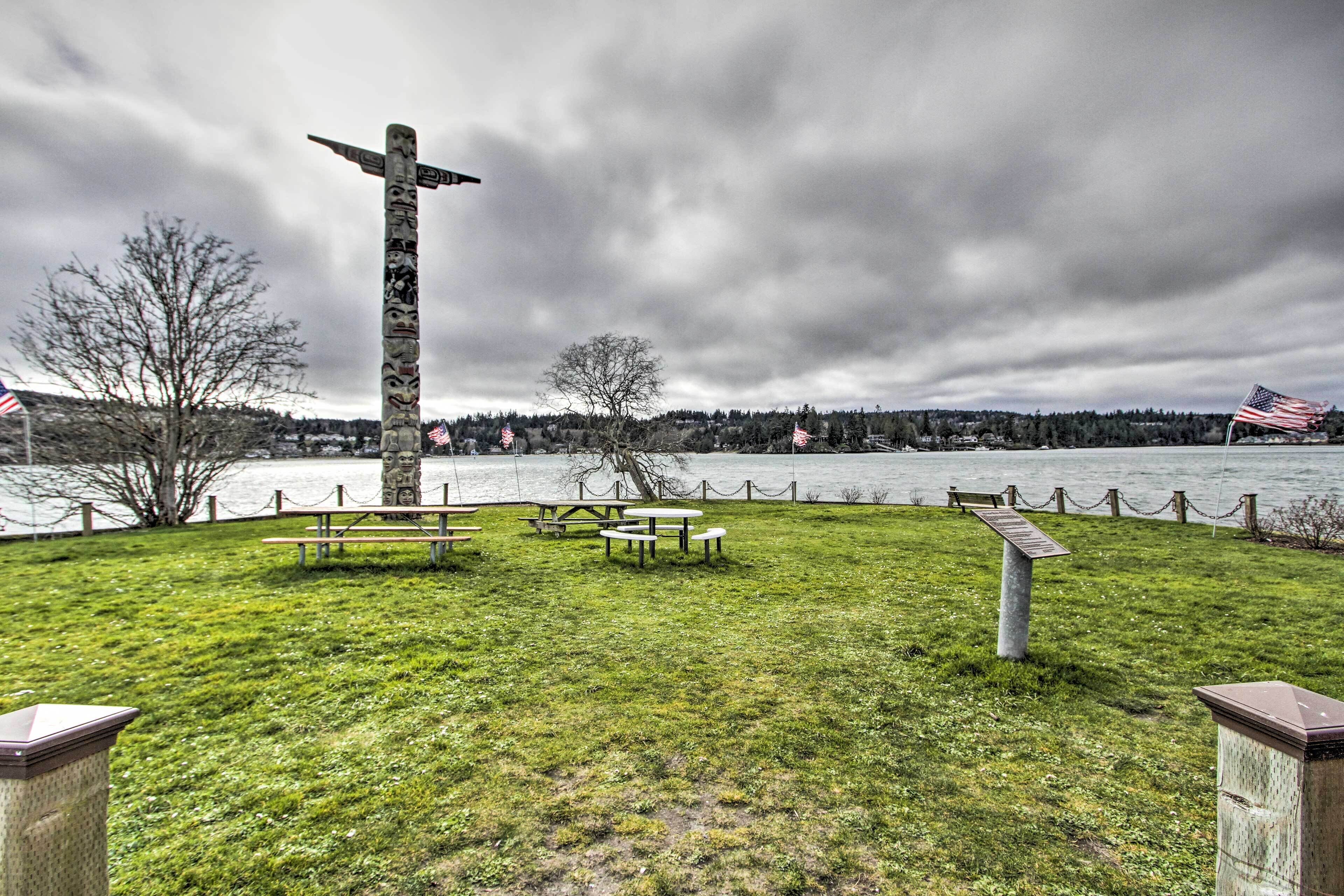 A park with picnic tables and a tall cross structure, overlooking a body of water and a forested area.