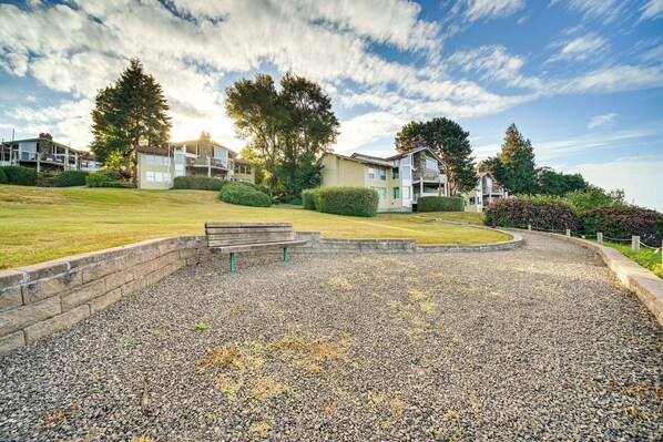 A residential area with a gravel driveway, a bench, and a grassy hill with trees. - Water Views & Marina Access: Port Ludlow Getaway (Port Ludlow)