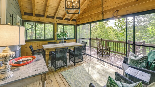 A wooden deck with a table and chairs, a hanging light fixture, and a view of trees through large windows. - Hike, Fish & Explore: Family Retreat in Highlands (Highlands)