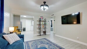Een woonkamer met een blauwe bank, een blauw vloerkleed, een televisie en een plafondventilator.
