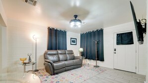 Un salon avec un canapé en cuir, une table basse en verre, un tapis à motifs, une lampe sur pied et un ventilateur de plafond.