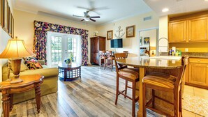 A spacious living area with a sofa, a coffee table, and a dining area with chairs and a kitchen counter. - 7 Mi to Disney World: Condo w/ 2 Balconies + Pools (Kissimmee)