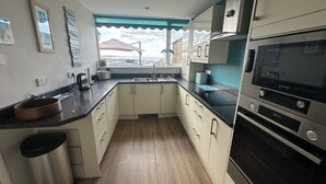 A modern kitchen with white cabinets, a black countertop, and a stainless steel trash can.