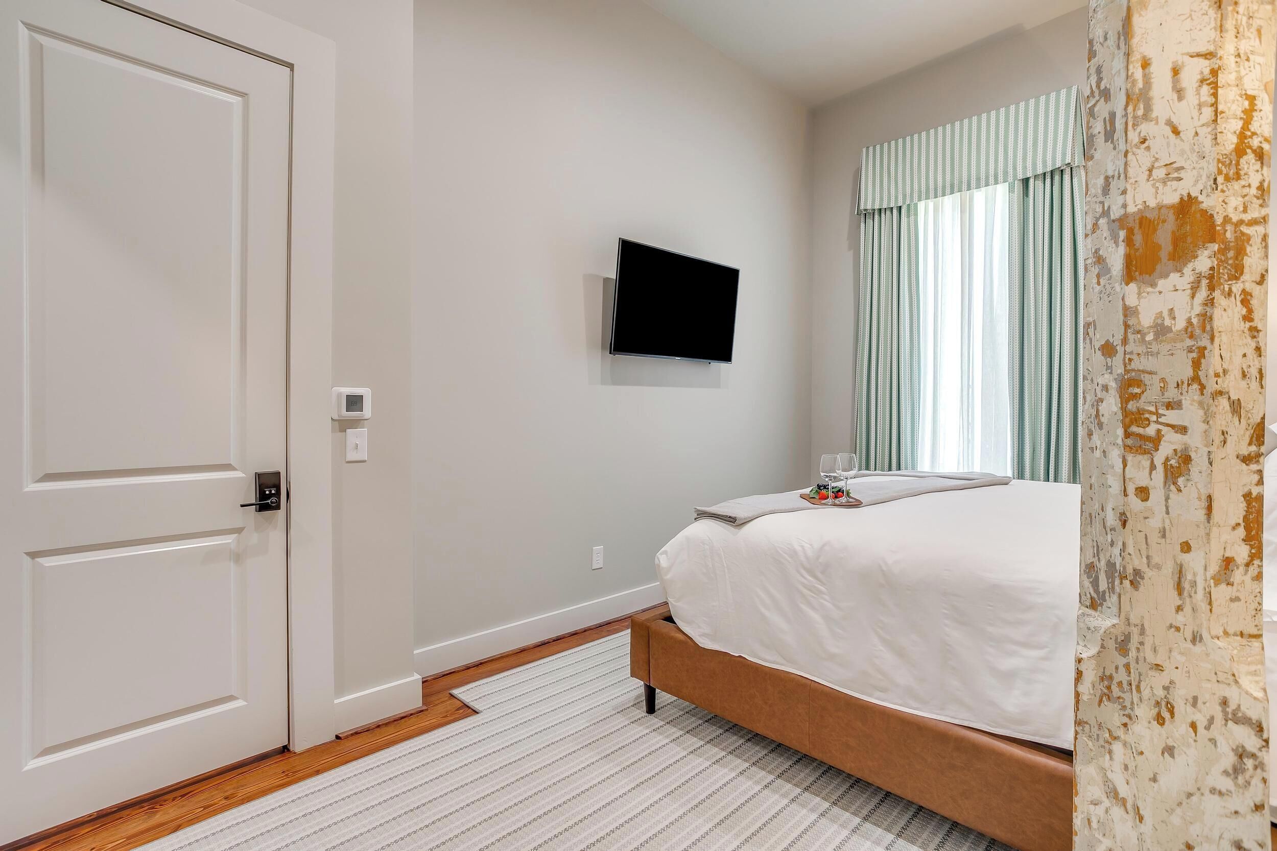 A hotel room with a bed, a television mounted on the wall, a door, and a window with curtains.