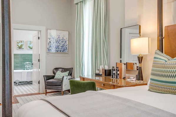A hotel room with a bed, a desk, a chair, a mirror, and a window with curtains.