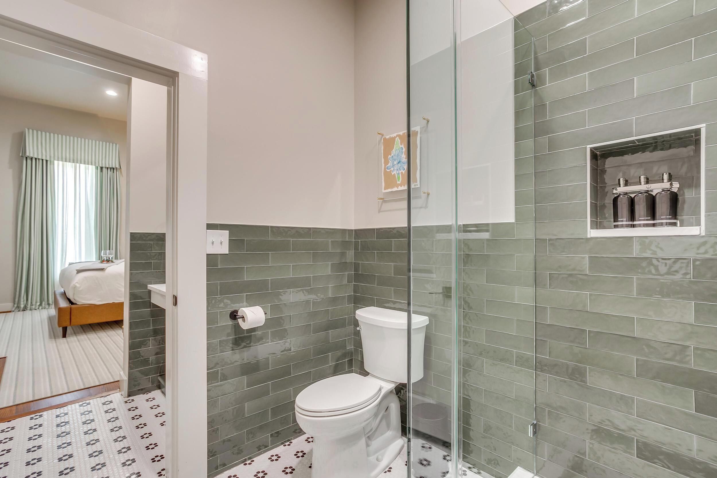 Une salle de bain avec une douche à parois de verre, des toilettes et une petite étagère contenant des articles de toilette.