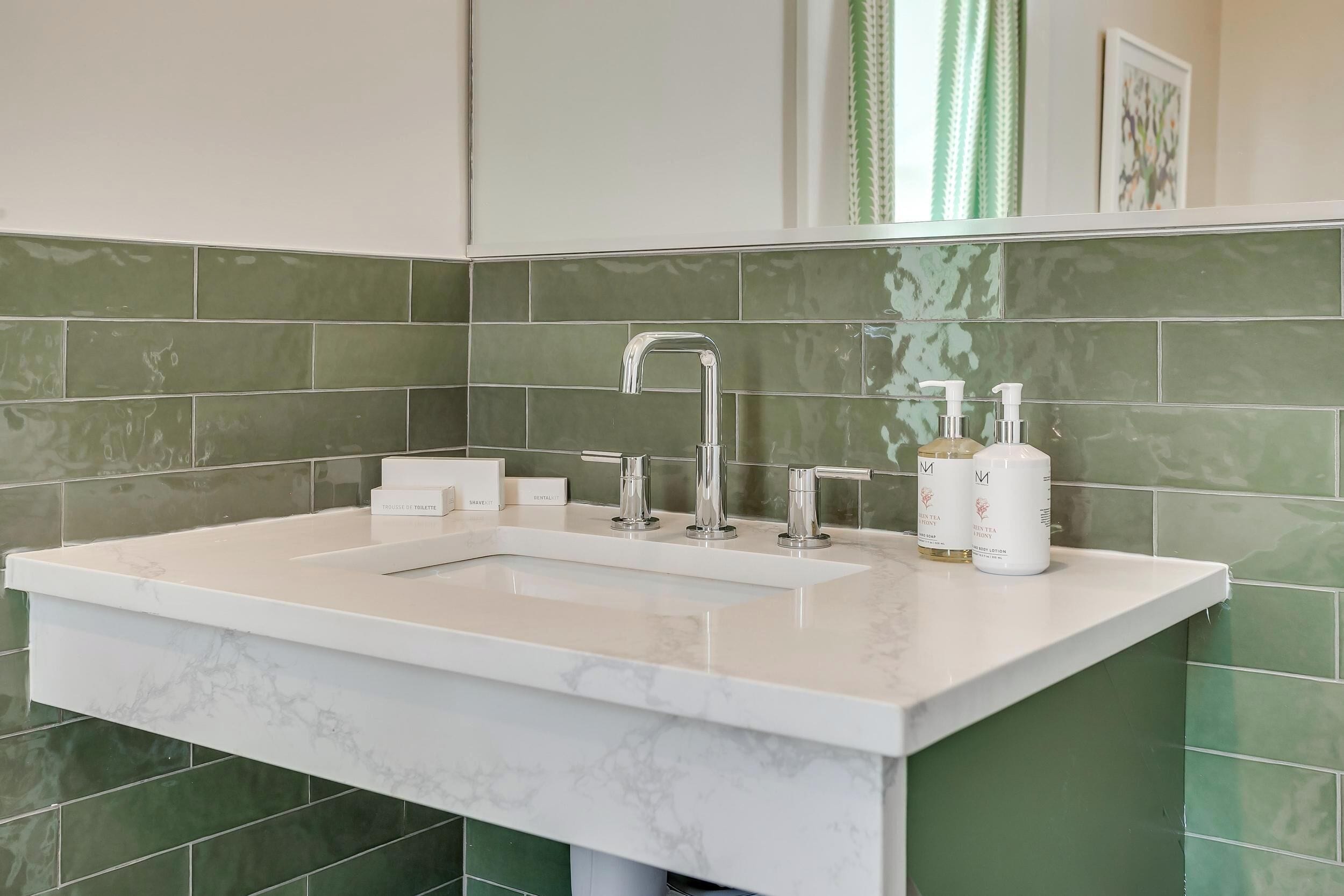 A bathroom with a white marble sink, green tiles, and a mirror above the sink.