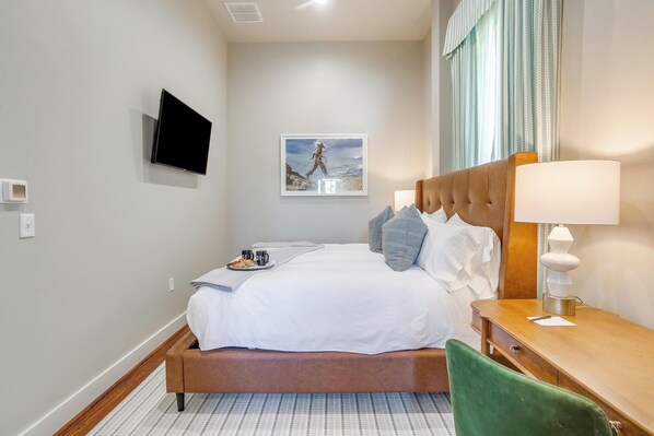A hotel room with a bed, a desk, a chair, a TV, and a picture on the wall. - Nutt House Hotel (Granbury)