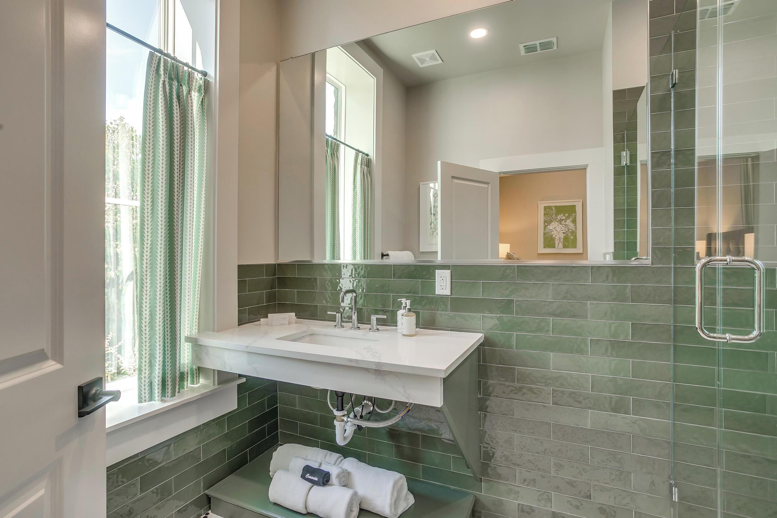 A bathroom with a white sink, green tiled walls, a large mirror, and a shower area.