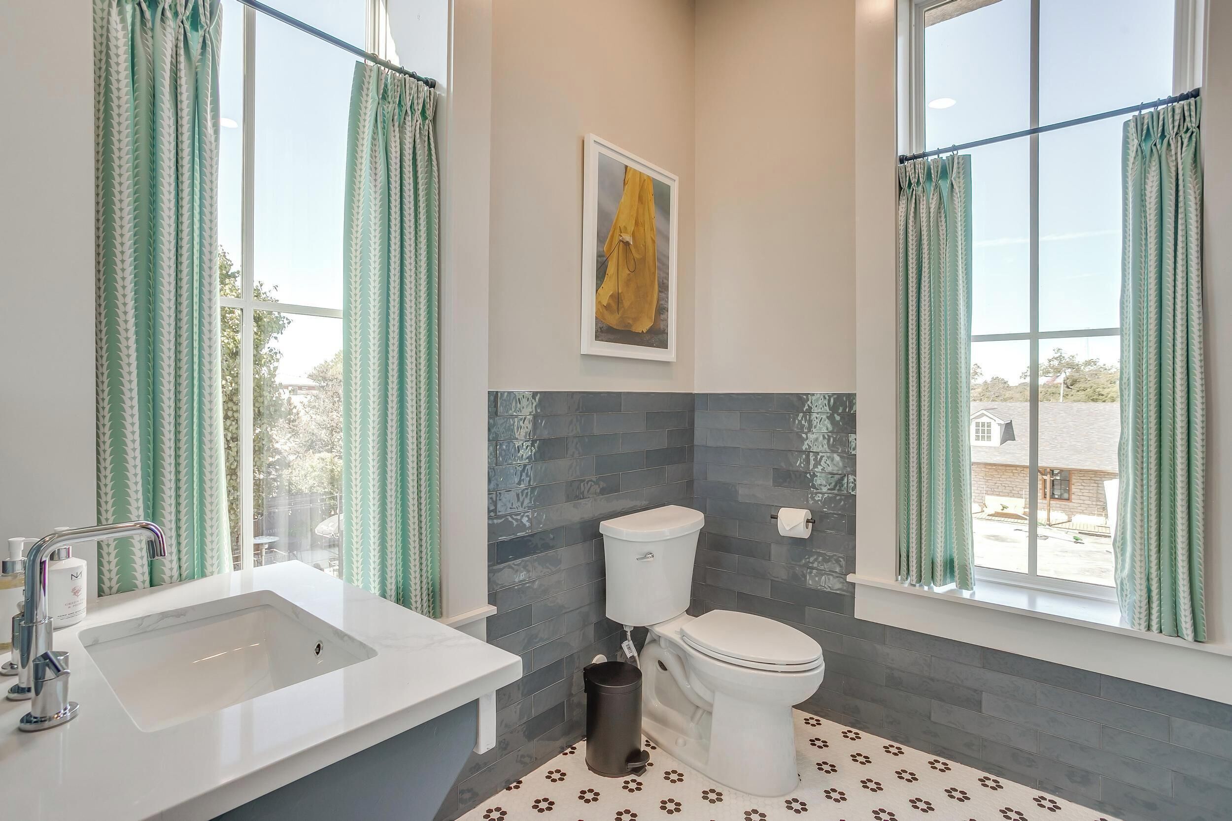 A bathroom with a white sink, a toilet, and a window with green curtains.