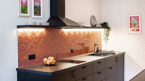 A modern kitchen with a herringbone-patterned backsplash, a black range hood, and a stainless steel sink.