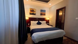 A hotel room with a bed, two bedside lamps, a headboard, and a door.