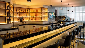 Un espace bar moderne doté d’un long comptoir, de tabourets et d’étagères remplies de bouteilles et de verres.