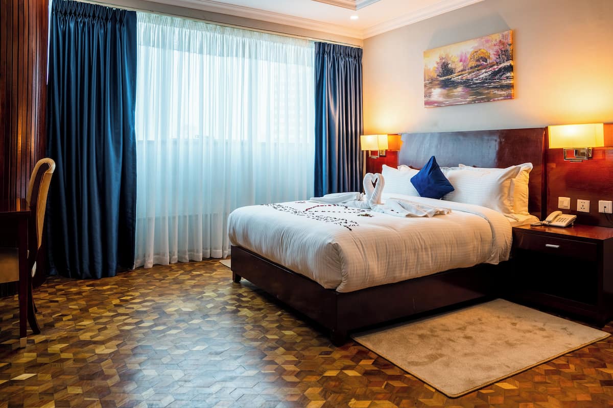 A hotel room with a large bed, a wooden floor, a desk, and a chair.
