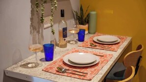 Une table à manger dressée avec des assiettes, des couverts et des verres, une bouteille et une plante en arrière-plan.