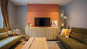 Un salon moderne doté d’un téléviseur à écran plat, de deux canapés, d’une table basse en bois et d’une petite table d’appoint agrémentée d’objets décoratifs.