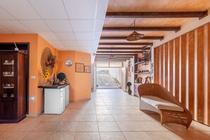 A hallway with a kitchen area, a wicker sofa, and a wooden wall with shelves.