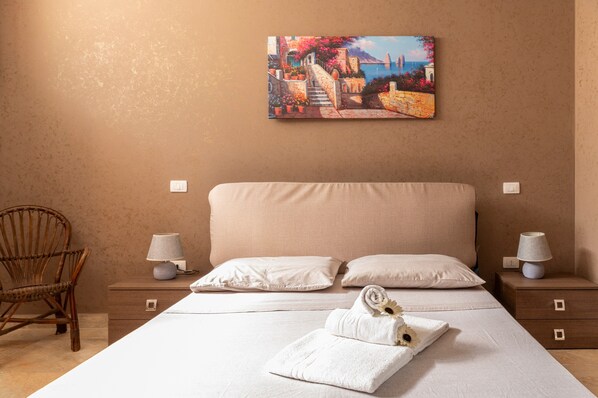 A bedroom with a bed, two nightstands, a chair, and a painting on the wall.