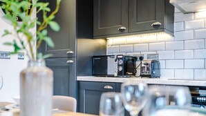 A modern kitchen with dark cabinets, a microwave, a coffee maker, and a plant on the counter. - Modern Flat in Central Leeds | Walk to City Centre (Leeds)
