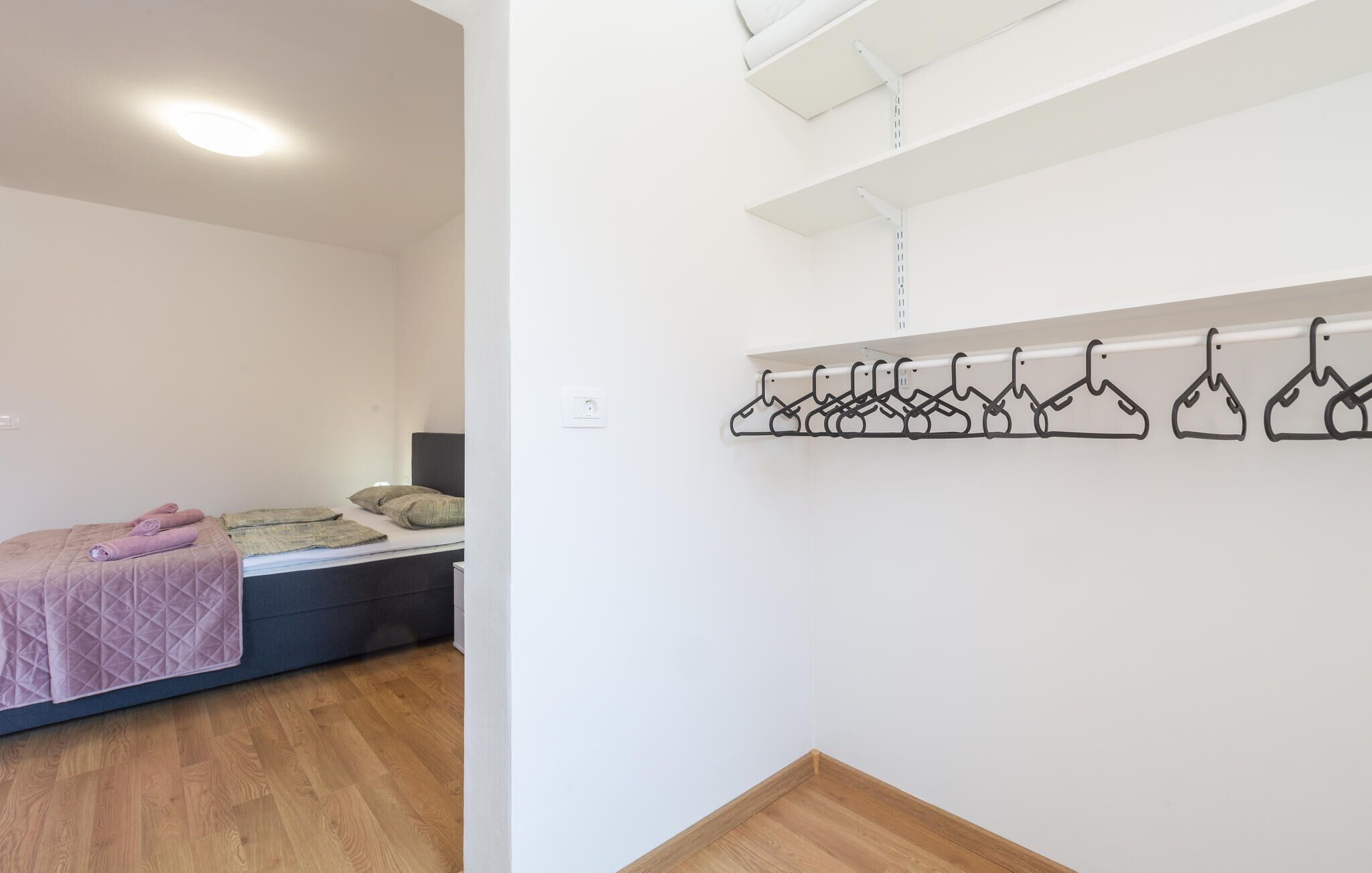 A bedroom with a bed, a bedside table, a hanging clothes rack, and a wooden floor.