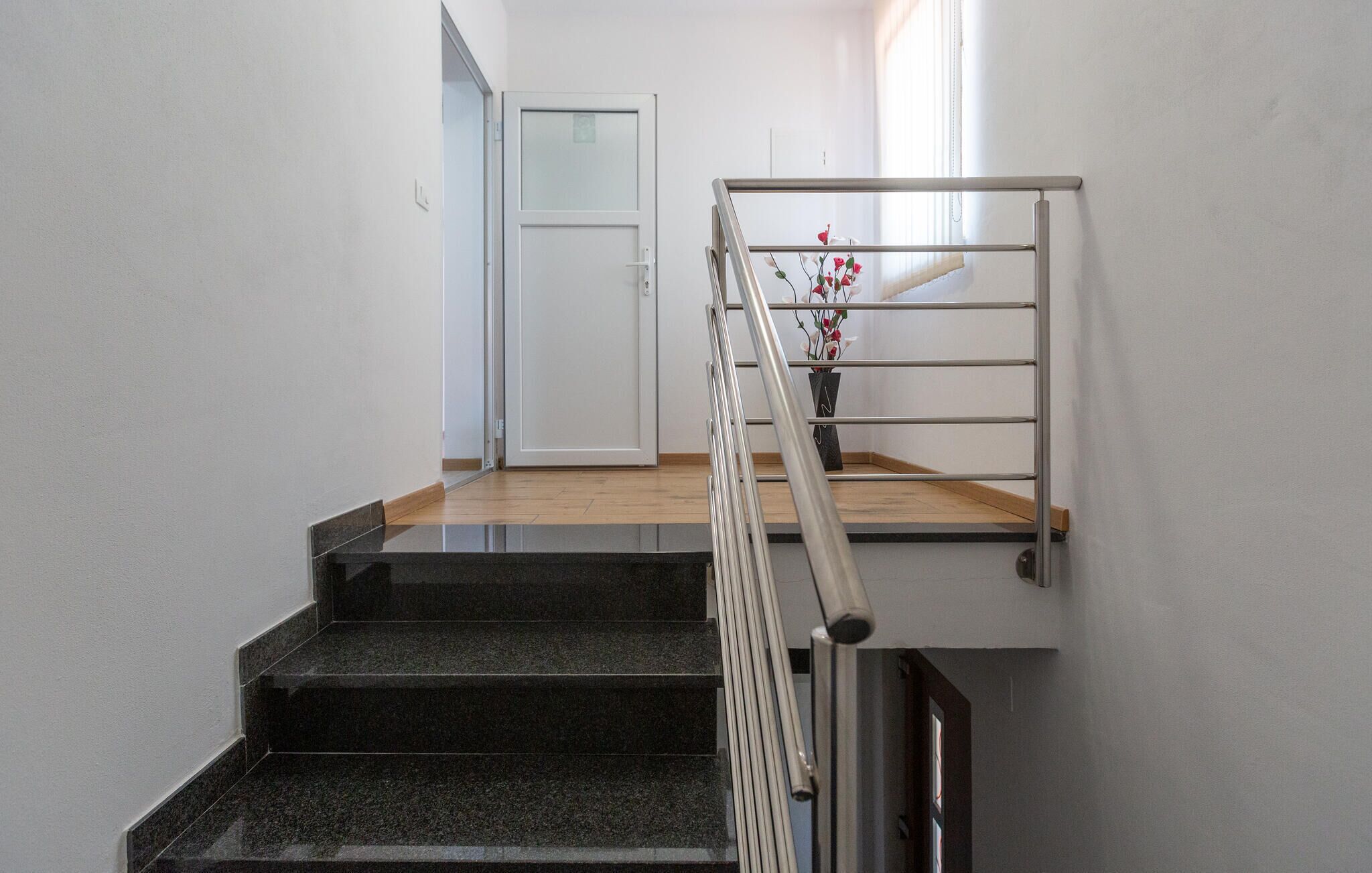 Uma escada com corrimão de metal, um patamar de madeira e uma porta ao fundo.