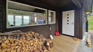 En stuga av trä med ett stort fönster, en dörr med ett titthål och en hög med ved utanför.